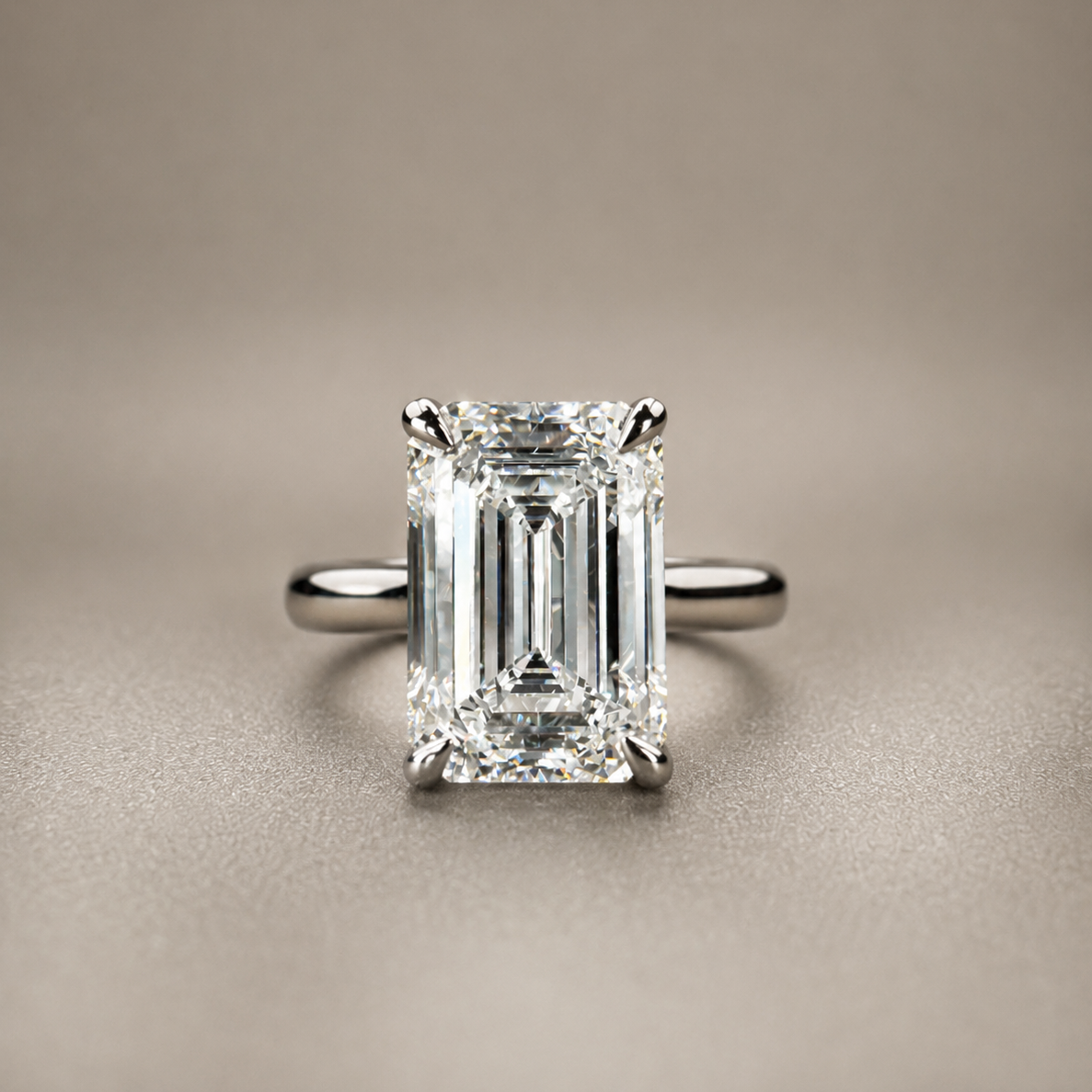 An emerald-cut diamond ring with a silver-toned band, centered on a textured beige background.