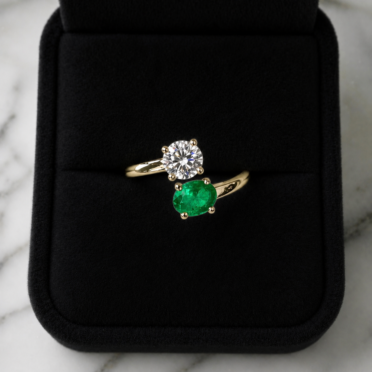 Gold ring with a diamond and emerald on a black cushion against a marble background