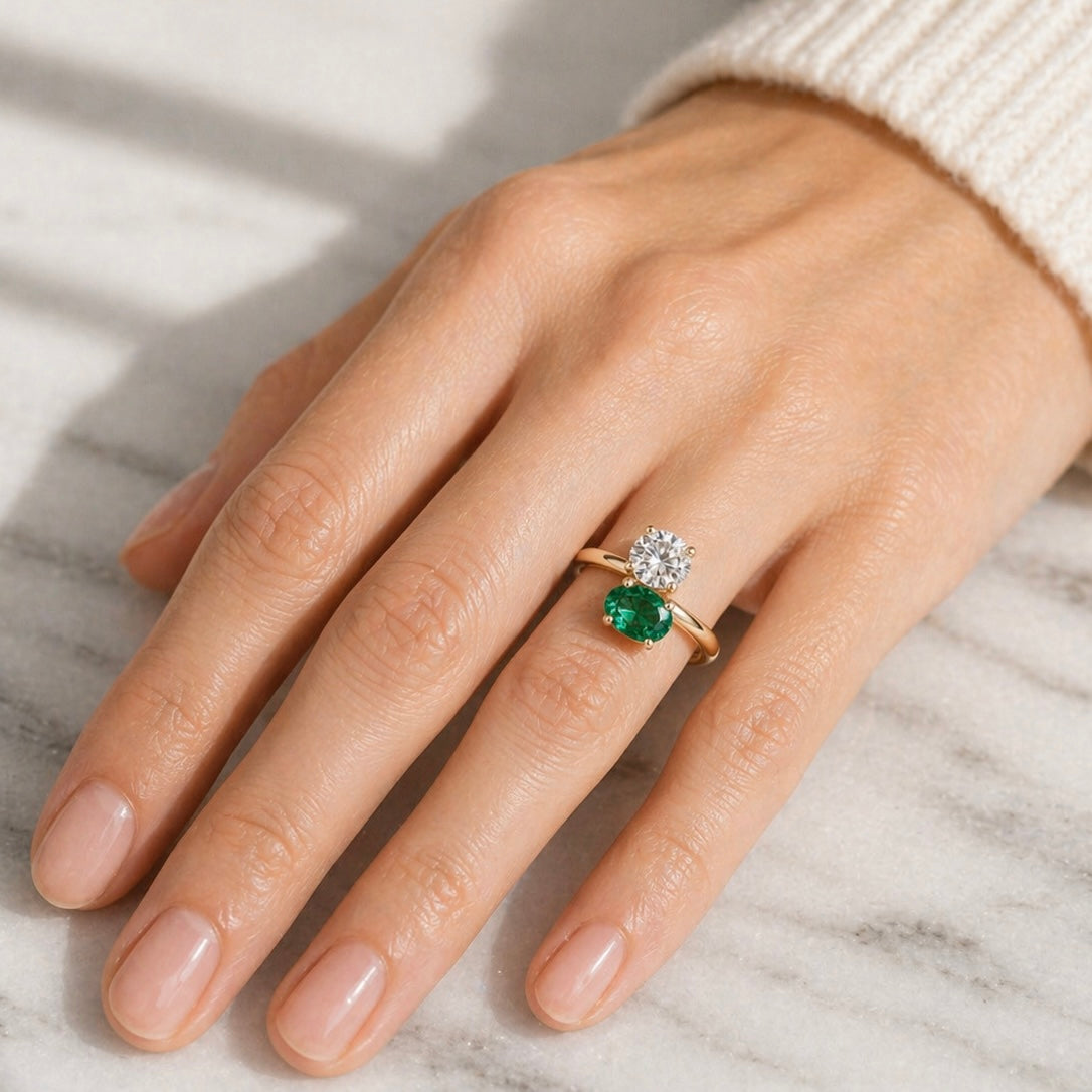 Hand wearing a ring with a green gemstone and diamond on a marble surface