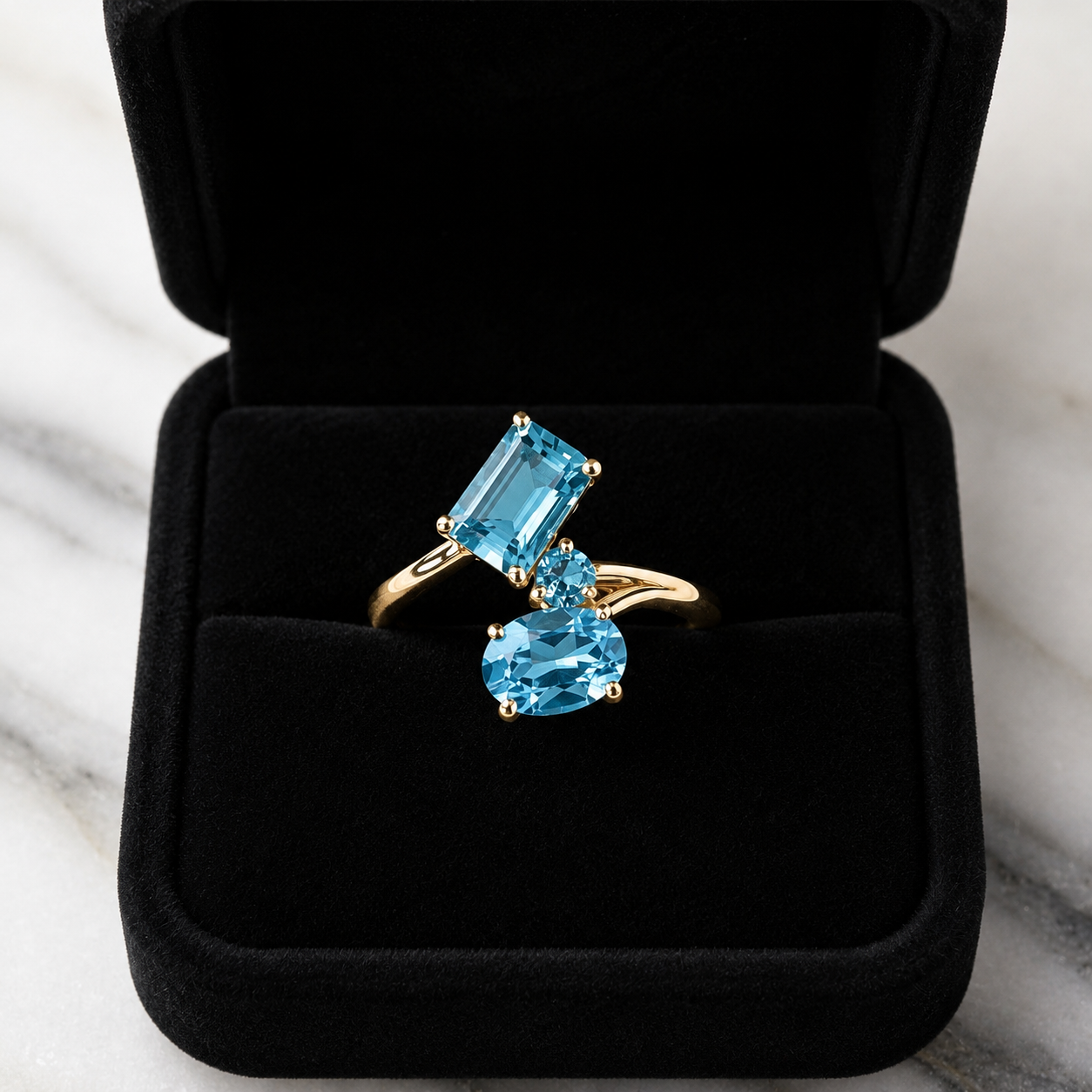 Gold ring with blue gemstones in a black jewelry box on a marble surface