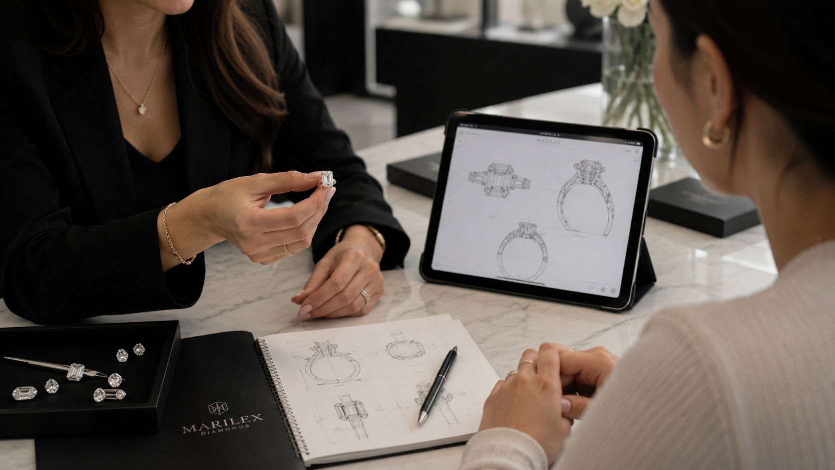 Two people discussing jewelry designs with a tablet and sketches on a table.