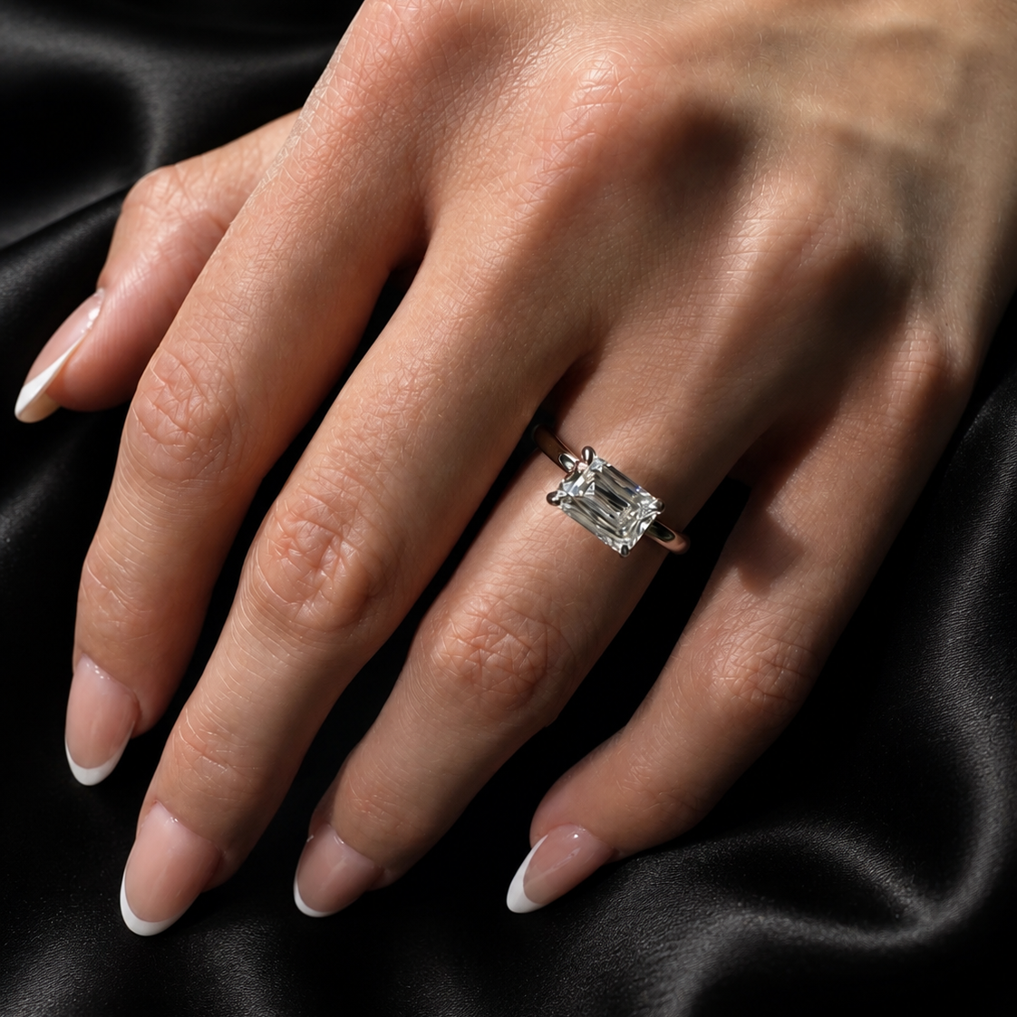 Hand wearing a diamond ring on black satin fabric