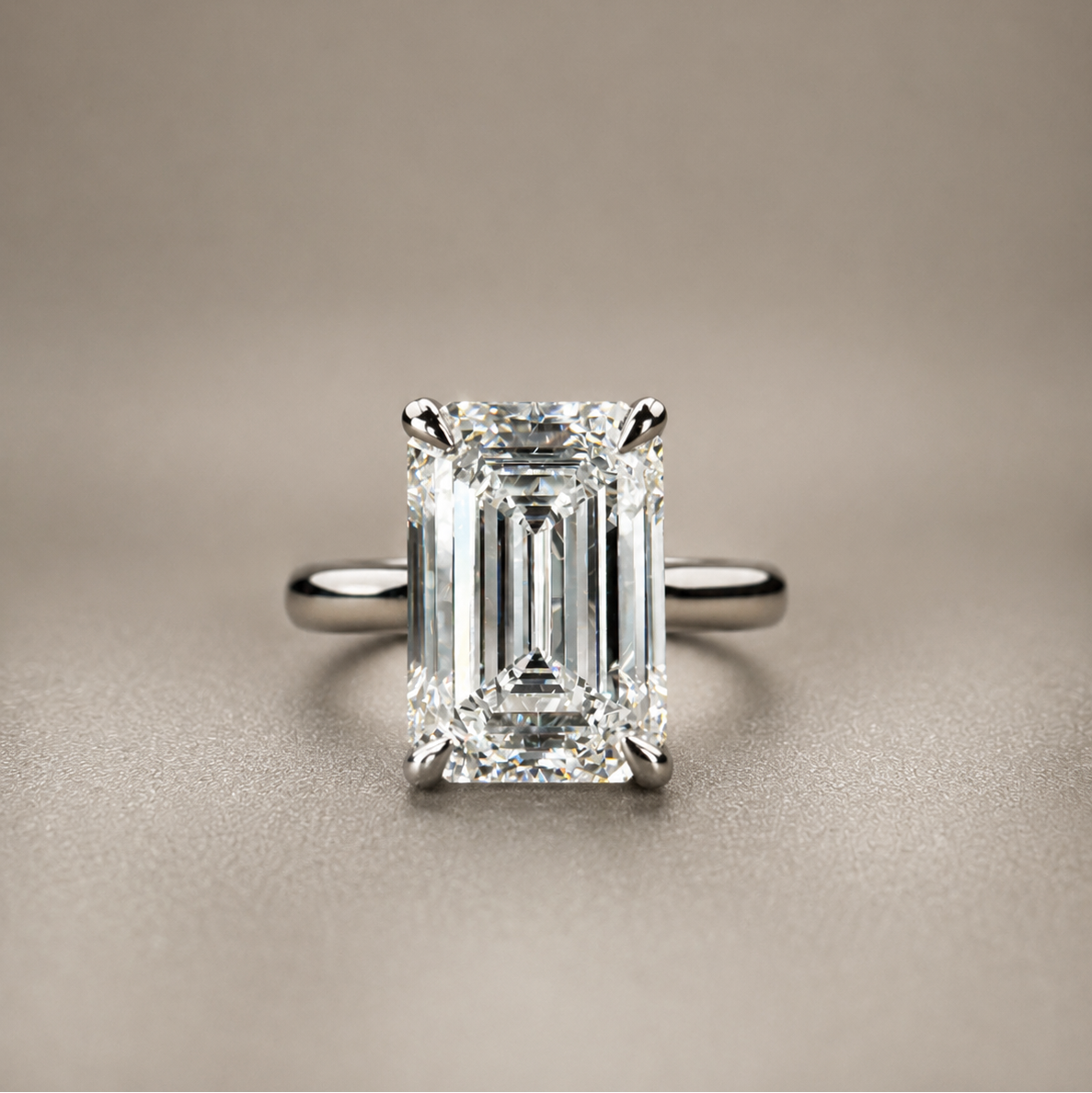 An emerald-cut diamond ring with a silver-toned band, centered on a textured beige background.