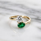 Gold ring with a diamond and emerald on a marble background