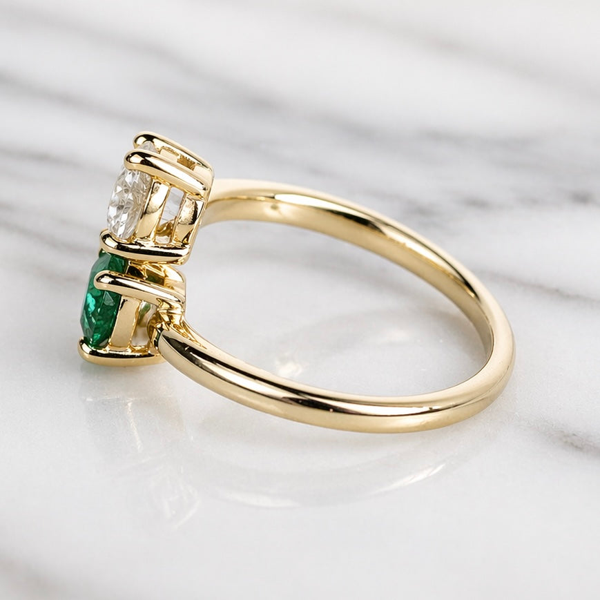 Gold ring with emerald and diamond on a marble background