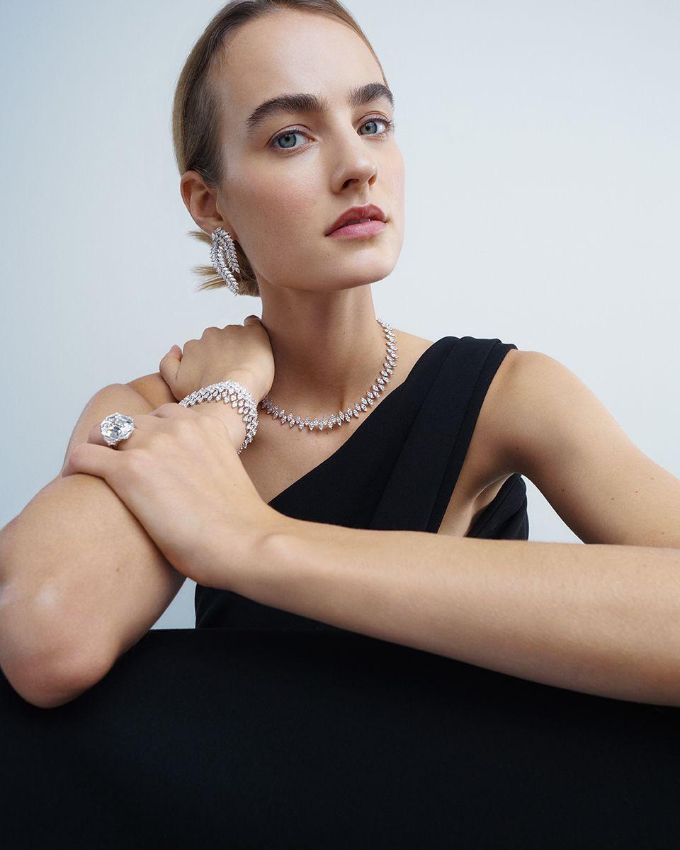 Woman wearing jewelry including a necklace, earrings, and ring against a plain background
