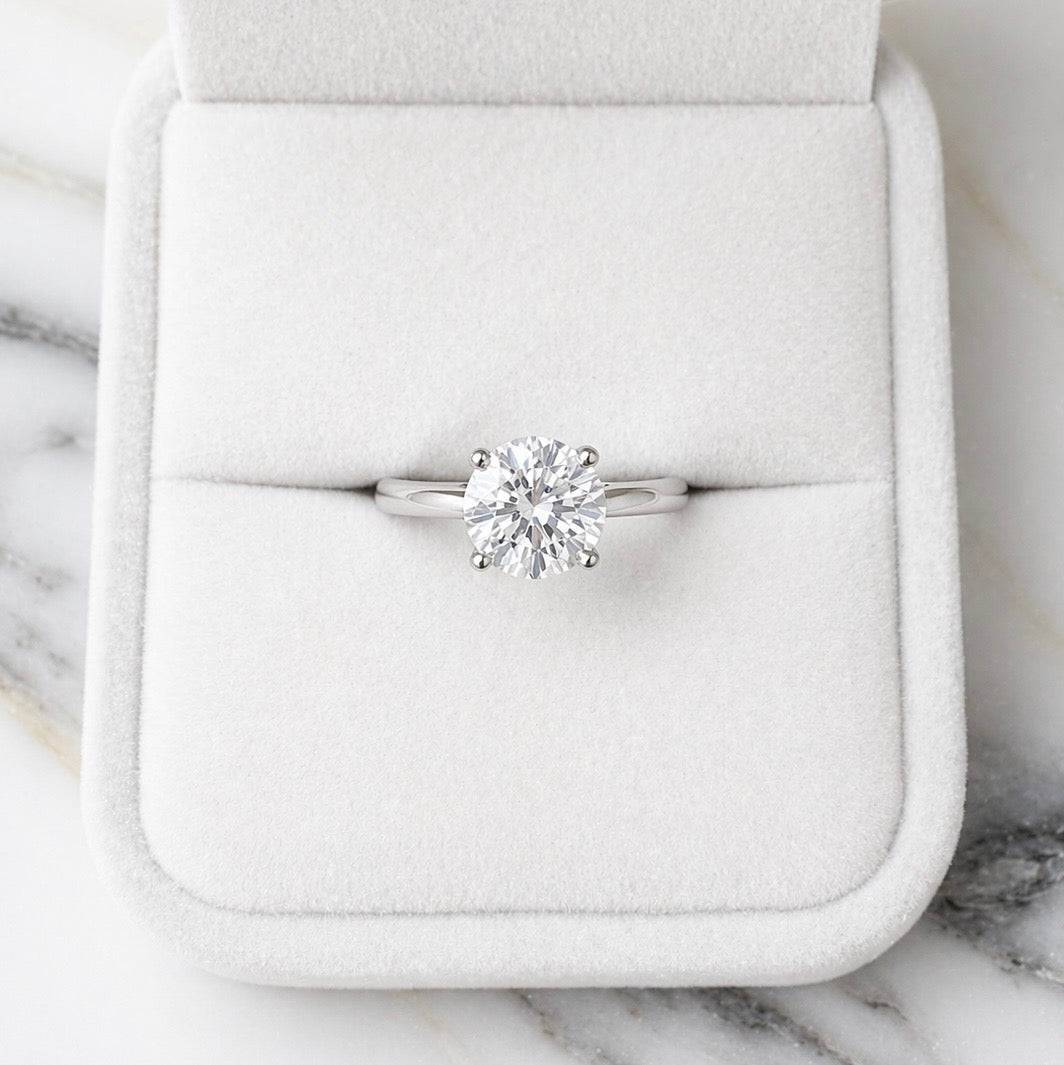 Diamond ring in a white jewelry box on a marble surface