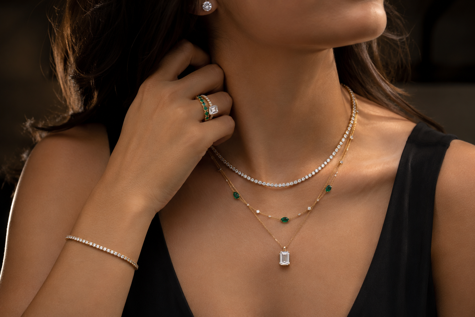 Close-up of a woman wearing multiple necklaces, rings, and a bracelet on a dark background.